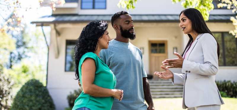 Two people standing in front of a house with a real estate agent.