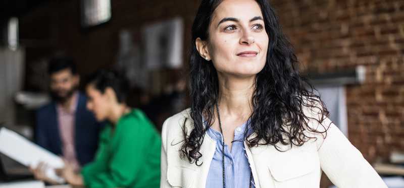 Adult in coffee shop wearing professional attire smiles.