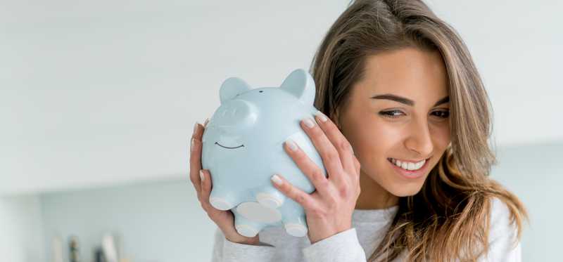 Woman smiling as she holds up piggy bank to her ear