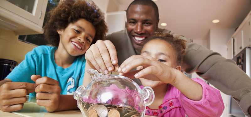 Adult and two children saving coins in piggy bank.