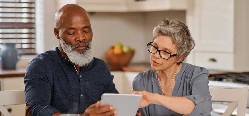 Two people looking at tablet and paperwork on kitchen table.