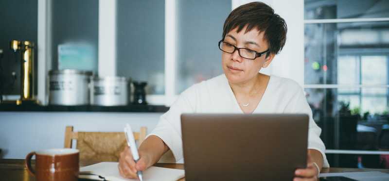 Person takes notes while sitting at table at home.