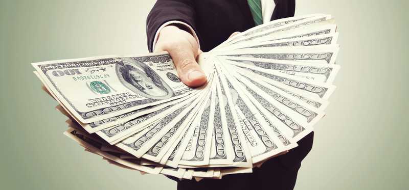 Man in business suit holding out a hand with a fan of cash