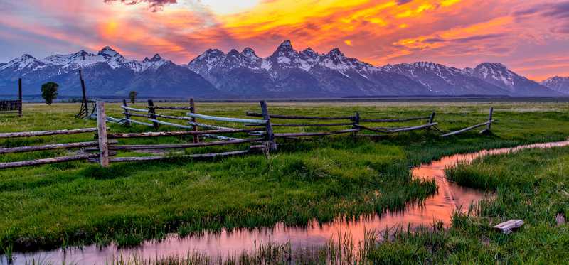 Stream running through green fields with mountains in the background in Wyoming