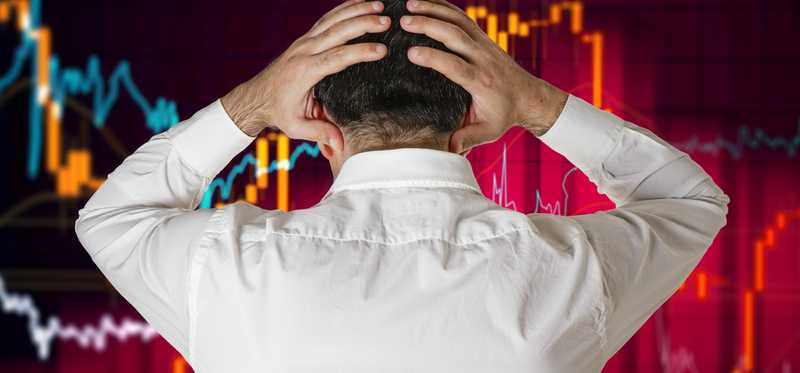 A distraught man with back turned, hands on his head, looking at a plunging line graph