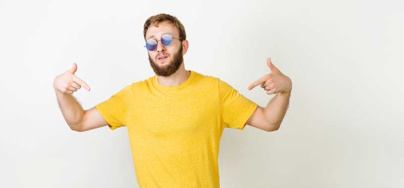 Bearded young man in yellow shirt and sunglasses points to himself
