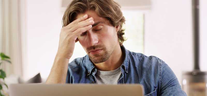 Man at computer touches forehead and closes eyes in dismay.