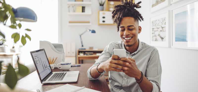 Man smiling and using his phone while seated at desk.