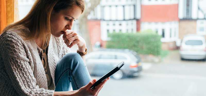 Woman sitting in windowsill and looking at phone
