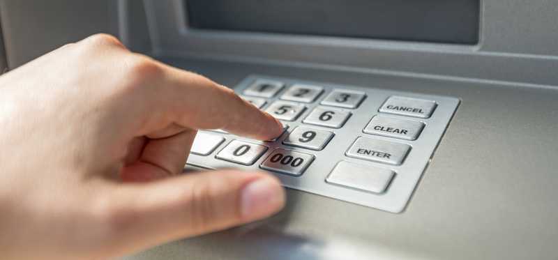 A hand is shown typing at an ATM keyboard