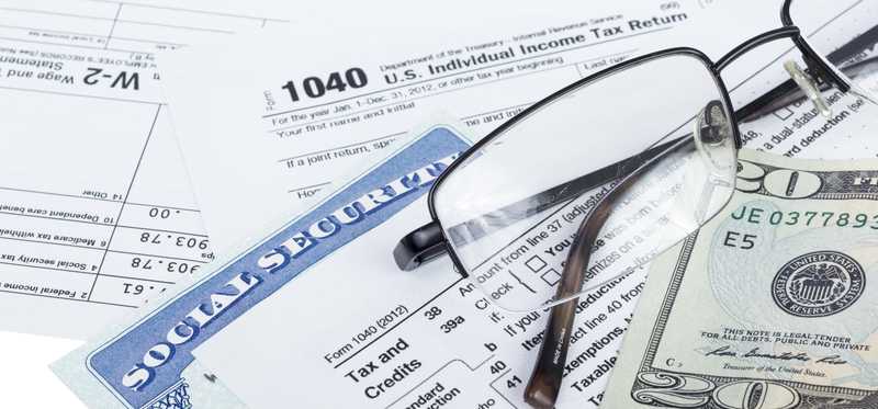 A Social Security card wedged between IRS tax forms and lying next a pair of glasses and twenty-dollar bill