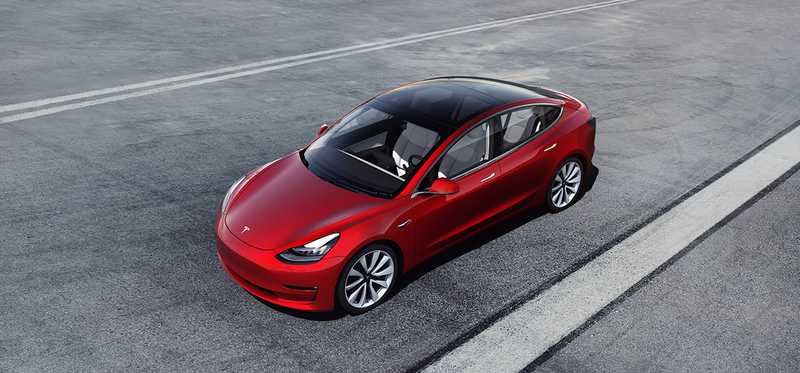 A red Tesla Model 3 on a wide road