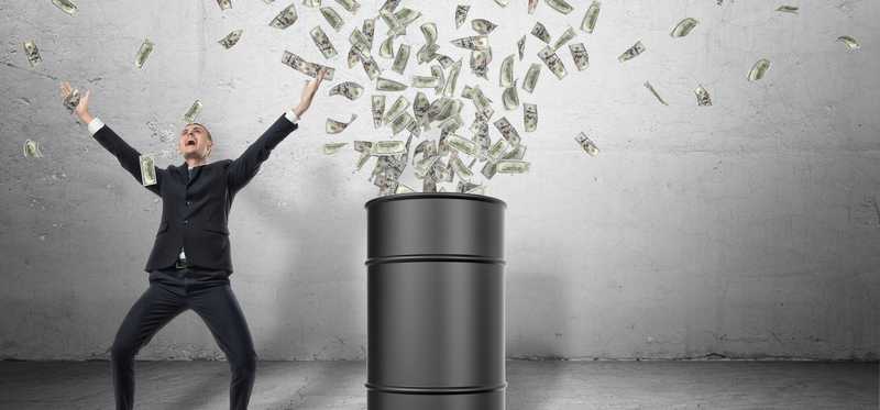 A barrel standing on a grey floor with money bursting out of it with a happy businessman in a celebrating next to it.