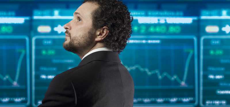 A businessman looking at a digital board containing stock quotes.