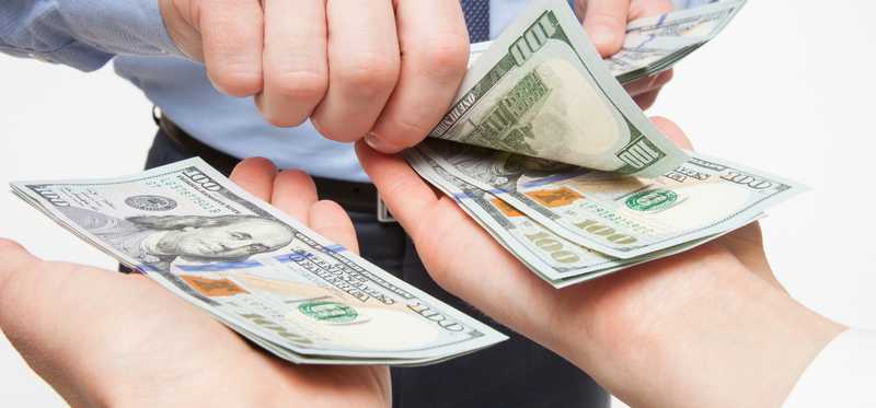 A businessman placing crisp one hundred dollar bills into two outstretched hands.