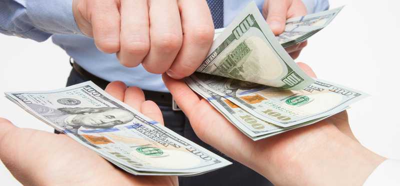 A businessman placing hundred dollar bills into two outstretch hands.