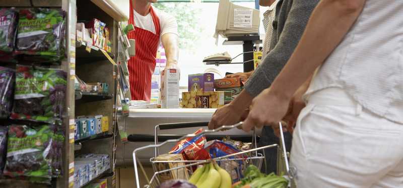 A consumer holding a handbasket of groceries while waiting in line to check out.