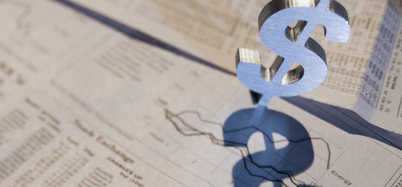A dollar sign standing up atop a financial newspaper.