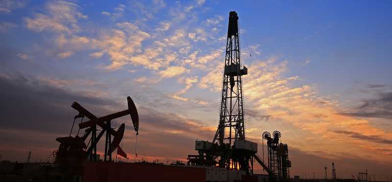 A drilling rig near some oil pumps with a nice sunset in the background