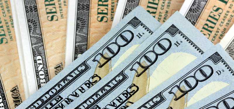 A fanned pile of hundred dollar bills lying atop Treasury bonds.