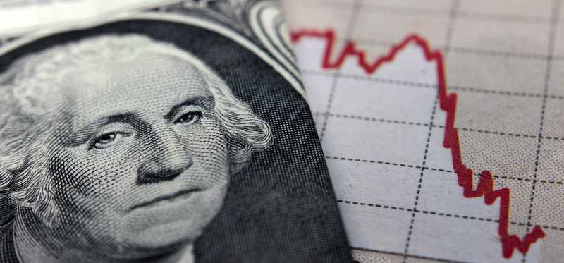 A folded dollar bill with George Washington’s face in the forefront next to a declining chart.