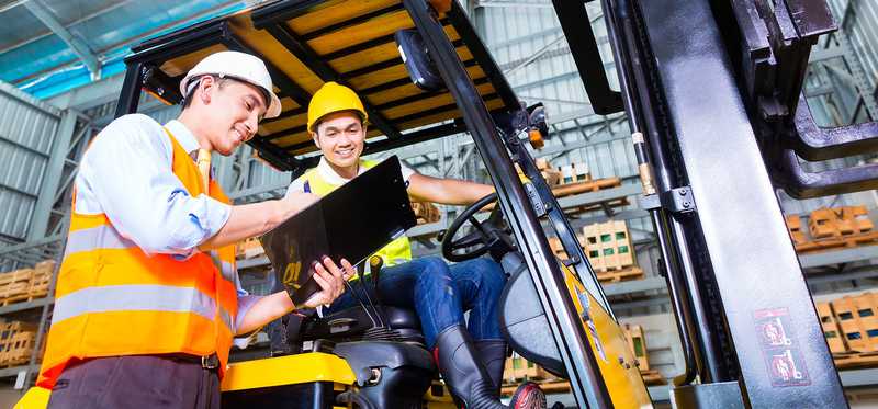 A forklift operator going over a checklist on a clipboard.