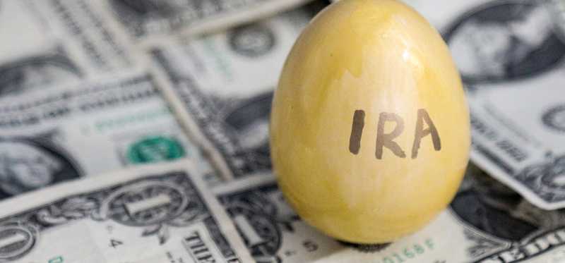 A golden egg with the word "IRA" written on it sitting on a messy bed of one dollar bills.