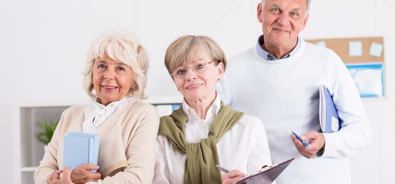 A group of three seniors with clipboards and notebooks in hand who appear intent on learning.