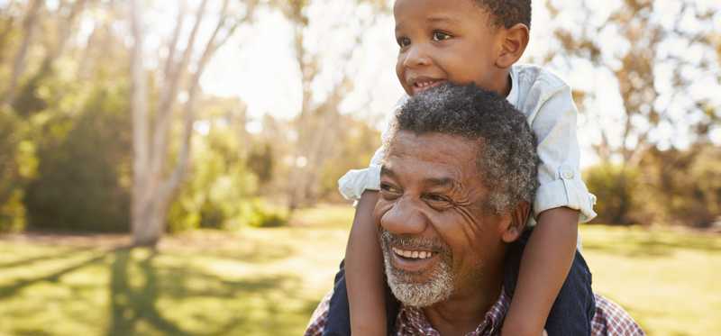 A happy grandson riding piggyback on his grandfather's back.