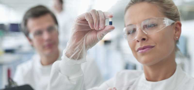 A female lab researcher examining a pill capsule.