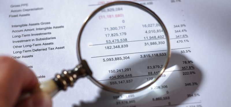 A magnifying glass being held over a balance sheet.