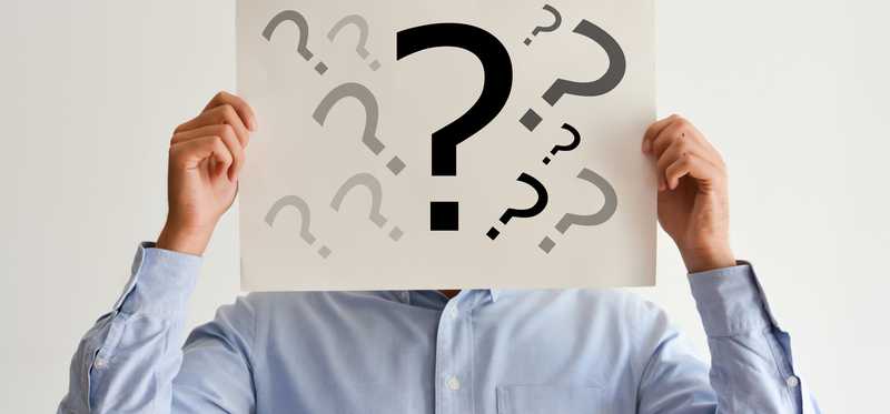 A man holding up a sign in front of his face that's covered in question marks.