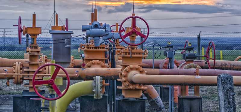 A natural gas field with pipeline valves and the sun setting in the background.