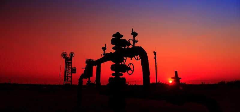 A natural gas well with pipelines at sunset.