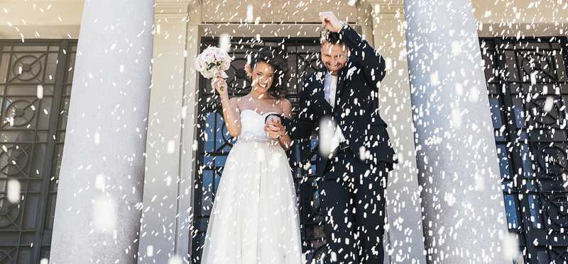 A newlywed couple being showered with rice while leaving the chapel.