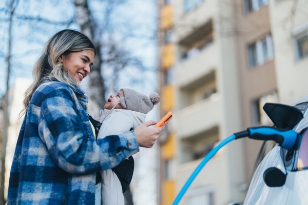 A parent holds an infant while charging an electric vehicle.