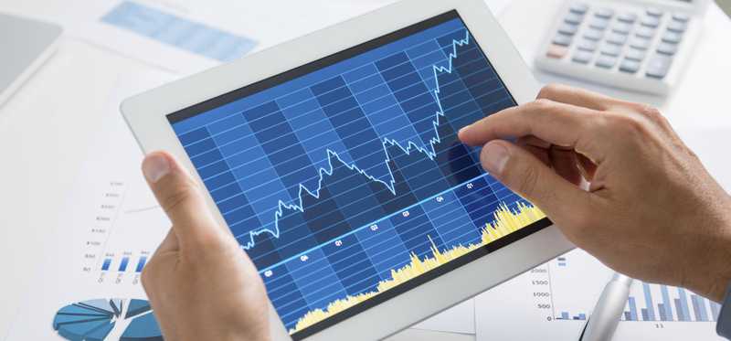 A person analyzing a volatile, but rising, stock chart on a tablet.
