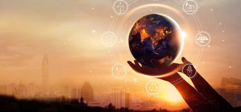 A person holding a globe with renewable energy images around it an a cityscape in the background.