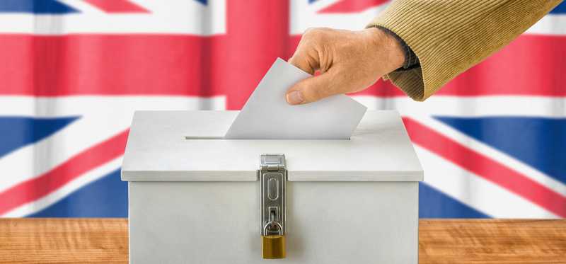 A person placing a ballot into a locked ballot box, with the British flag in the background.