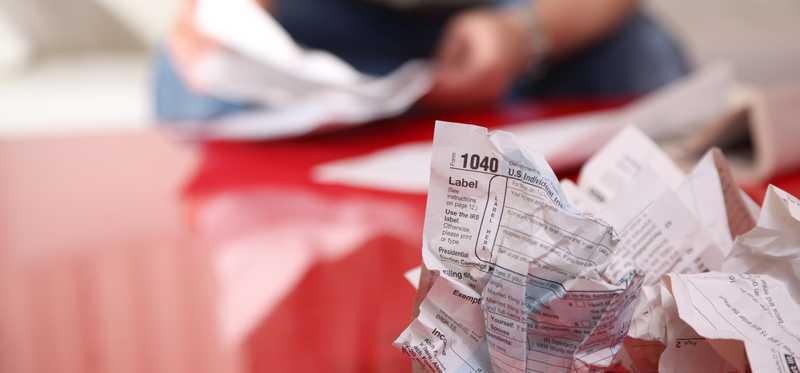 A person preparing their taxes, with a crumpled up IRS tax form on the table.