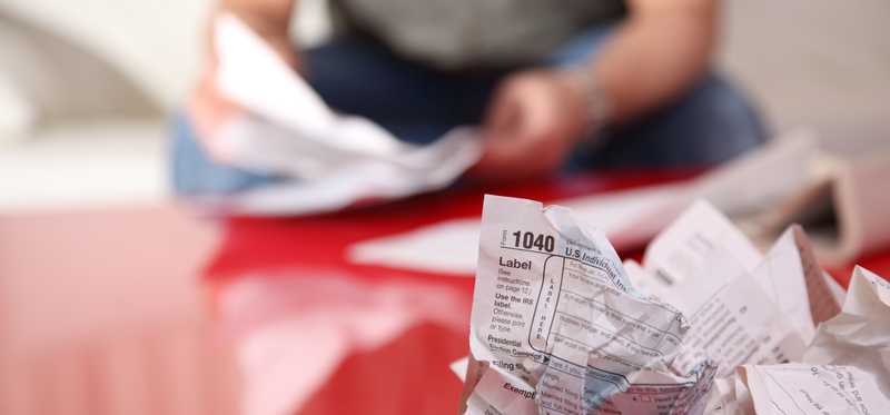 A person preparing their taxes, with a crumpled IRS tax form on the table.