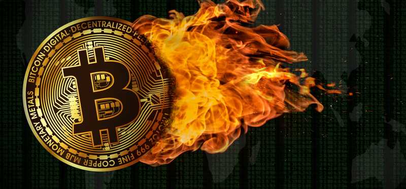 A physical gold coin marked with the bitcoin B that's on fire.
