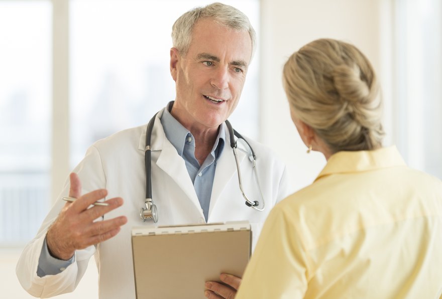 A physician holding a clipboard who's having a discussion with a female patient.