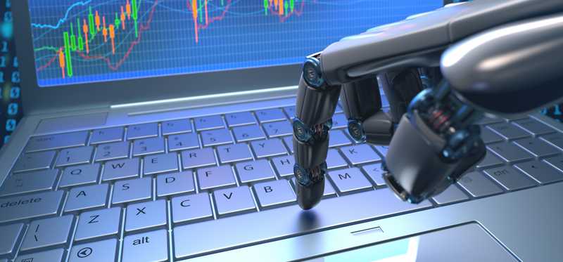 A robotic hand touching a keyboard, with a stock chart on the laptop screen.