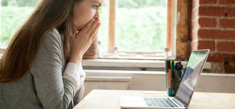 A female looking at her laptop in shock with hands over her mouth.
