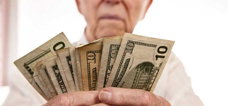 A senior man counting a fanned stack of cash bills in his hands.