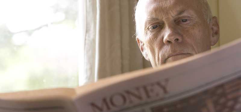 A senior man reading a section of the newspaper entitled Money.