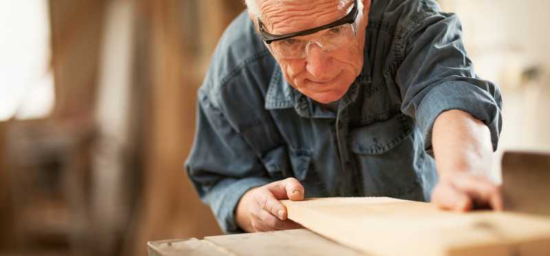 A person wearing eye protection while using a machine to cut a piece of wood.