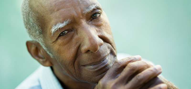 A senior man with his hands interlocked in front of his face in deep thought.