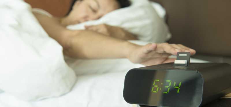 A sleepy woman turning off her digital alarm clock.